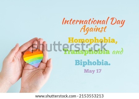 Concept International Day Against Homophobia, Transphobia and Biphobia. May 17. Stop Homophobia. Heart with rainbow LGBT flag in the hands on blue background. Royalty-Free Stock Photo #2153553213