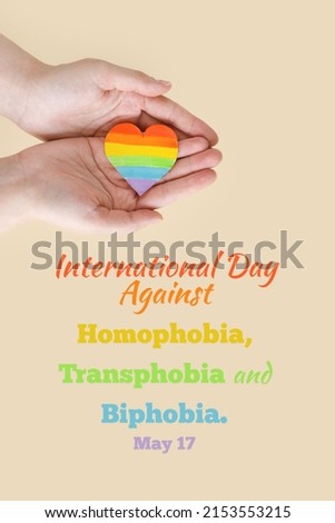 Concept International Day Against Homophobia, Transphobia and Biphobia. May 17. Stop Homophobia. Heart with rainbow LGBT flag in the hands on beige background. vertically photo Royalty-Free Stock Photo #2153553215
