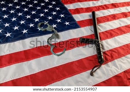 silver metal handcuffs and black rubber police baton over full-frame background of US flag on flat surface