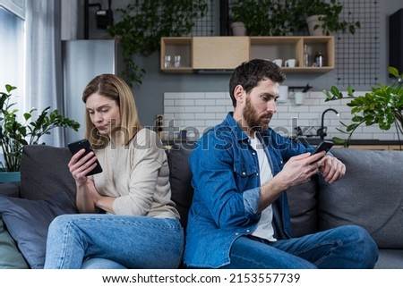 Conflict, quarrel. Man and woman, couple, family sitting on the couch with their backs to each other with phones, do not talk to each other, do not pay attention, busy with phones Royalty-Free Stock Photo #2153557739