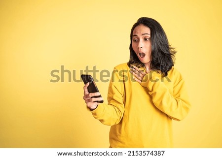 asian woman shocked while looking at her mobile phone on isolated background