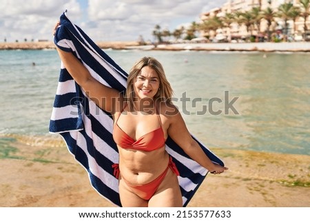 Young hispanic woman wearing bikini holding towel at seaside