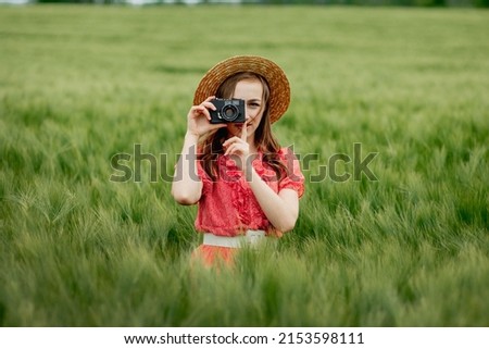 Woman in the middle of the field takes a photo with a retro camera.