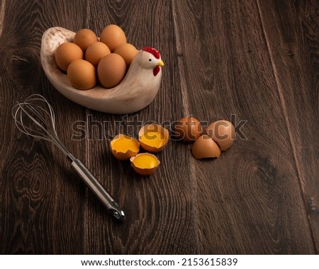Eggs, egg yolks, shells and a whisk on a dark wood background with copy space