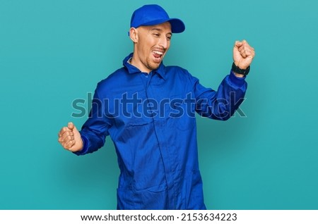 Bald man with beard wearing builder jumpsuit uniform dancing happy and cheerful, smiling moving casual and confident listening to music  Royalty-Free Stock Photo #2153634223