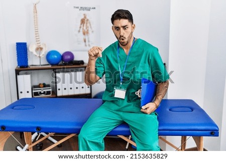 Young physiotherapist man working at pain recovery clinic pointing down with fingers showing advertisement, surprised face and open mouth 