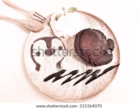 molten lava chocolate cake with whipping cream and cute  penguin cartoon from coco powder as decoration on wooden dish, retro effect filter or instagram filter 