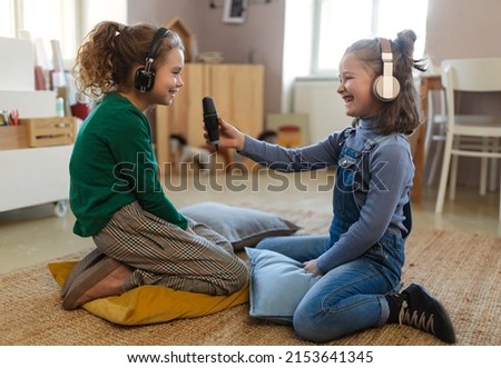 Little girls with headphones and microphone taking an interview, having fun and playing at home. Royalty-Free Stock Photo #2153641345