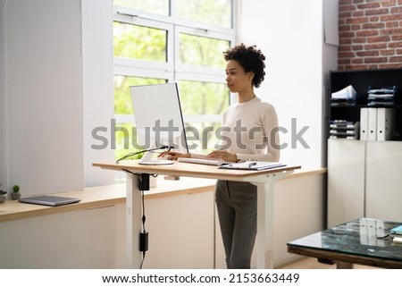 Woman Using Adjustable Height Standing Desk In Office For Good Posture Royalty-Free Stock Photo #2153663449