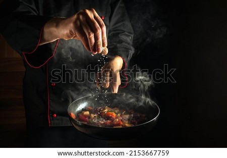 Professional chef adds salt to a steaming hot pan. Grande cuisine idea for a hotel with advertising space. Royalty-Free Stock Photo #2153667759
