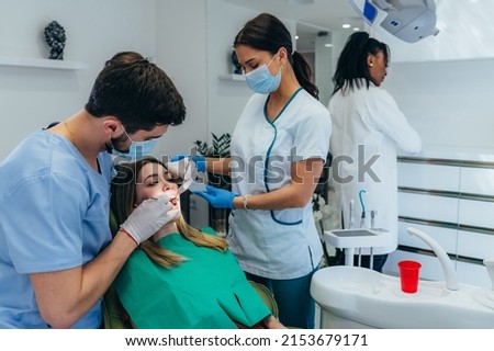 Male dentist with a help of his assistant fixing teeth of a woman patient in the dentists chair. Dentist examining patient teeth and having a dental checkup at dental clinic. Royalty-Free Stock Photo #2153679171