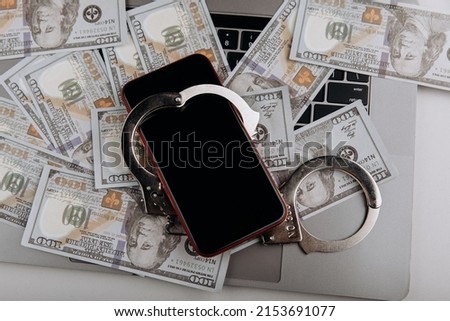 Smartphone on banknotes with handcuffs on a keyboard. Top view. Digital crime concept