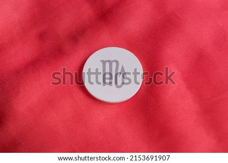 shooting of a white wooden circle on a red background engraved with a zodiac sign, in particular the sign of Scorpio