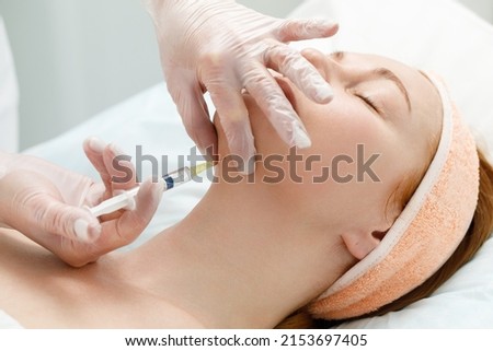 Cosmetologist performs the chin lift procedure by injecting beauty injections. Doctor injecting hyaluronic acid into the ching of a woman as a facial rejuvenation treatment. Royalty-Free Stock Photo #2153697405