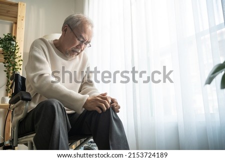 Asian senior elderly man feel painful and suffering from injured leg. Attractive mature male patient having a knee problem while sit on wheelchair in living room at home. Health care Insurance concept Royalty-Free Stock Photo #2153724189