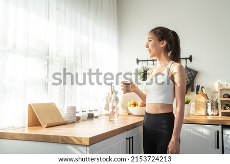 Asian beautiful woman in sportswear drink water after exercise at home. Young thirsty active sport girl takes a sips of clean mineral natural in cup after workout for health care in kitchen in house. Royalty-Free Stock Photo #2153724213
