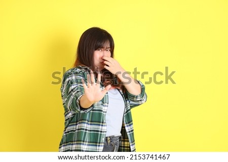 The chubby Asian woman standing on the yellow background with the casual clothes.