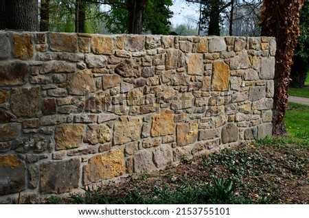 an old stone wall is being reconstructed between the two plots. the stones are dismantled and re-glued to the cement mortar. stonemason builds a wall in the park. the joints are repaired and the bush Royalty-Free Stock Photo #2153755101