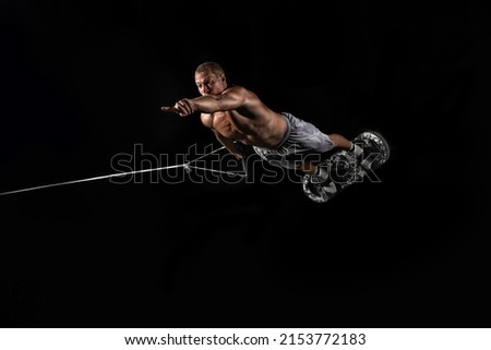 A man is engaged in trampoline jumping on a rubber board and pointing his index finger at a black background.