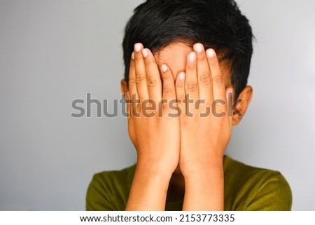 Little Asian boy closing his face with hands as if playing hide and seek or scared of something.