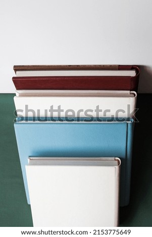 Four stylish photo books with a leather cover, white, burgundy, brown and blue, of different thicknesses, lie on a green tabletop, against a white wall, indoors.