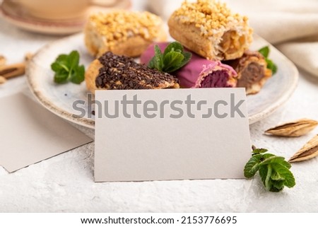 Gray paper business card and set of eclair on gray concrete background. side view, close up, selective focus, still life. Breakfast, morning, concept.
