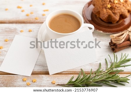 White paper business card mockup with cup of coffee and cake on white wooden background. Blank, side view, still life.