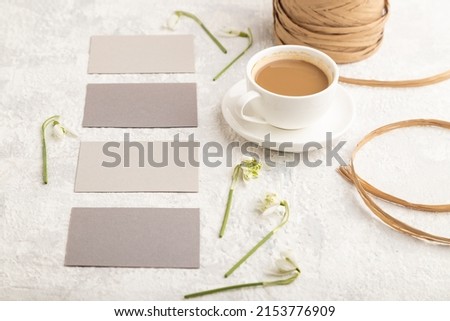 Gray paper business card mockup with spring snowdrop galanthus flowers and cup of coffee on gray concrete background. Blank, business card, side view, copy space, still life. spring concept.