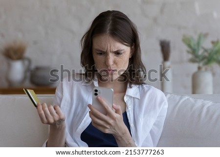 Puzzled confused shopper girl facing problems with online payments, blocked account, electronic wallet, overspend budget, holding credit card, mobile phone, staring at screen, getting bad news Royalty-Free Stock Photo #2153777263