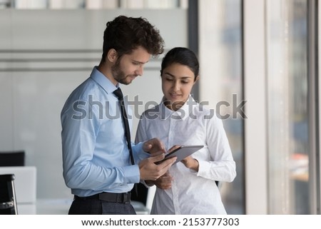 Two busy diverse young business coworkers in formalwear using tablet computer, watching online presentation. Employees discussing startup project. Indian professional consulting colleague expert Royalty-Free Stock Photo #2153777303