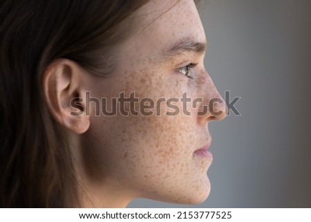 Thoughtful freckled teenage girl facial close up side portrait. Pretty young model woman clean face with fresh clean spotted skin looking away, thinking. Natural beauty, skincare, cosmetology concept