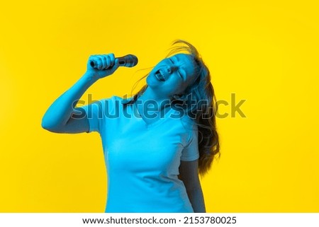 Singer, musician. Beautiful young girl with freckles on her face isolated on yellow background in neon. Concept of wow emotions, facial expression, youth, aspiration. Trendy vivid, bright colors.