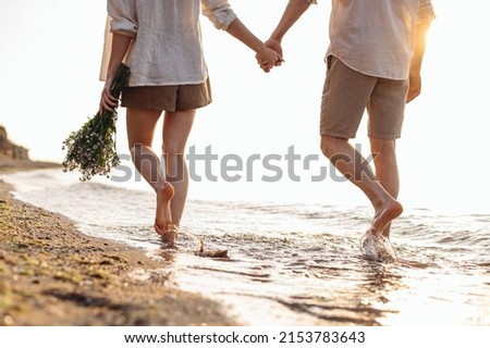 Cropped close up back view young couple two family man woman in white clothes hold flowers bouquet hand walk in water waves at sunrise over sea beach ocean outdoor seaside in summer day sunset evening Royalty-Free Stock Photo #2153783643