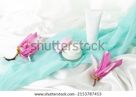 cream jar and plastic container mockup with magnolia flowers on white satin background