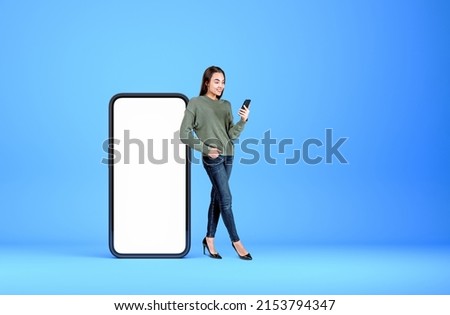 Smiling woman with mobile phone, full length near device mock up copy space display, light blue background. Concept of social media and communication