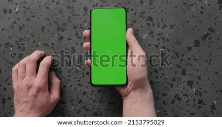 Top view man hand use smartphone with green screen on concrete background, wide photo