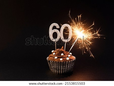 Happy 60th Birthday Card image, or for 60th anniversary, silver number 60 in a birthday cupcake with chocolate frosting, and gold sparkler , silver sprinkles, silver cup case, a black background