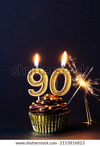 Happy 90th Birthday Card Image, gold number 90 candles, with gold sparkler, golden cup case with gold sprinkles on chocolate frosting, black background