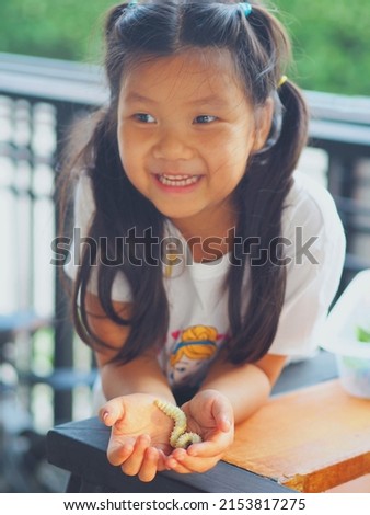 Young little girl gently hold giant cassava silk worm in hand cheerfully. Selective focus.