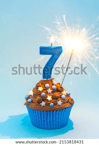 Happy 7th Birthday Card Image, blue number 7 candles, and sparkler, blue cup case, chocolate frosting, blue sprinkles, blue background 