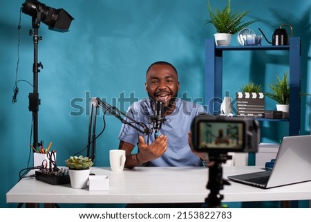 Exalted content creator in studio looking at dslr live video podcast setup during online live show. Vlogger talking with audience in excitement in front of recording digital video camera.
