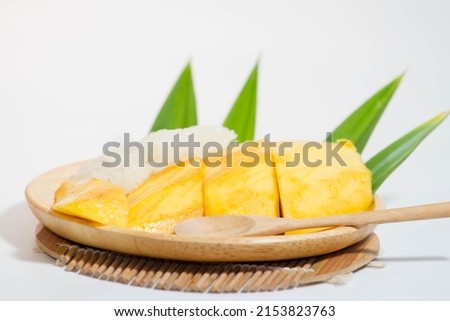 Mango sticky rice in a wooden plate and a wooden spoon, white background.