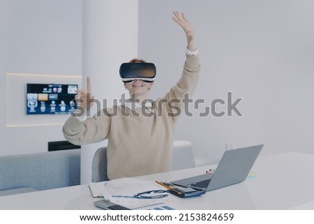 Young european woman in VR headset in office. Student of futuristic college. Girl working on project in cyberspace. Concept of being in virtual reality and simulation in education. Royalty-Free Stock Photo #2153824659