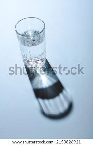 Glass of clean water under the bright light throwing a hard shadow on blue background.
