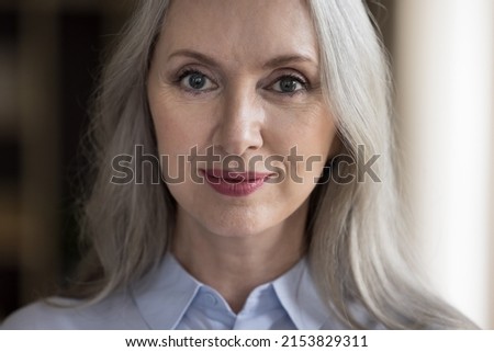 Positive confident beautiful mature woman head shot close up portrait. Pretty grey haired retired lady, middle aged model with makeup looking at camera, posing indoors. Elderly age concept