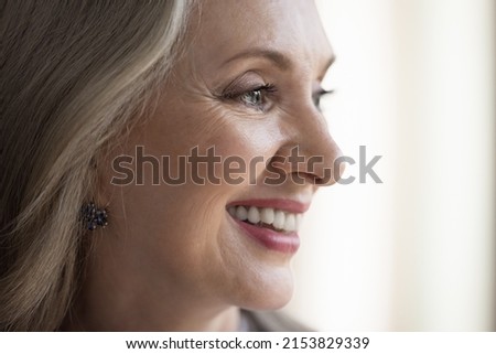 Happy dreamy mature grey haired lady face with makeup close up. Pretty retired woman, pensioner looking away with toothy smile. Elderly age, dental care concept. Cropped shot side portrait