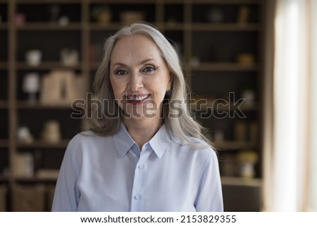 Happy pretty mature grey haired business woman head shot portrait. Positive satisfied retired lady, grandmother looking at camera, smiling, posing indoors. Video call talk screen