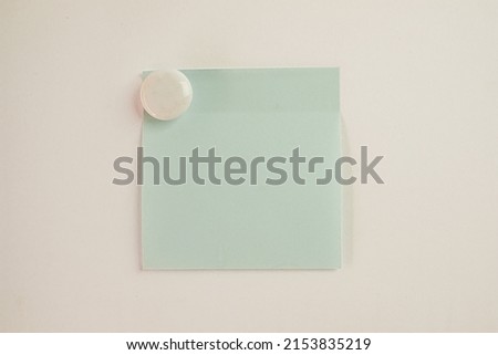 Light Blue sticky note with White circle magnet on white wall background.