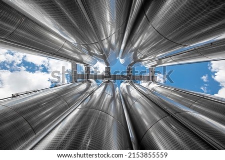 A row of stainless steel fermentation wine tanks against clouds and a blue sky. Steel wine tanks for wine fermentation at a winery. modern wine factory with large shine tanks for the fermentation. Royalty-Free Stock Photo #2153855559