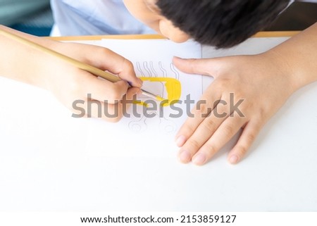 Close up of cute Asian little boy drawing and painting his imagination monster character on white art paper at home. Child brain development and art therapy concept.